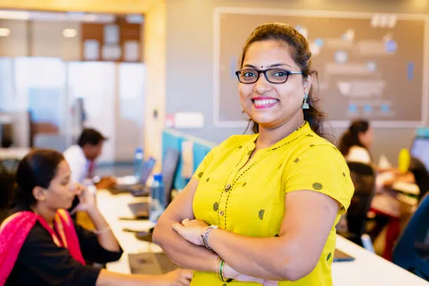 Professional woman smiling in a classroom setting during an online ECCE course in Mumbai, with students attending training sessions in the background.