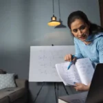 Woman attending online teacher training courses while studying educational notes during a virtual learning session.